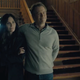 Courteney Cox and Greg Kinnear stand side by side in front of a long, wooden staircase in a scene from horror comedy series Shining Vale.